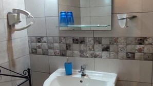 Un bagno con un lavabo su piedistallo, uno specchio e uno scaffale con flaconi blu.