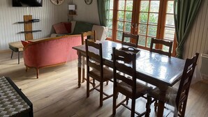 Un coin repas avec une table et des chaises en bois, un canapé avec des coussins, un téléviseur fixé au mur et une fenêtre avec des rideaux.