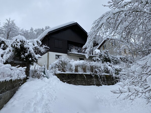 A snow-covered house with a black roof and a balcony.