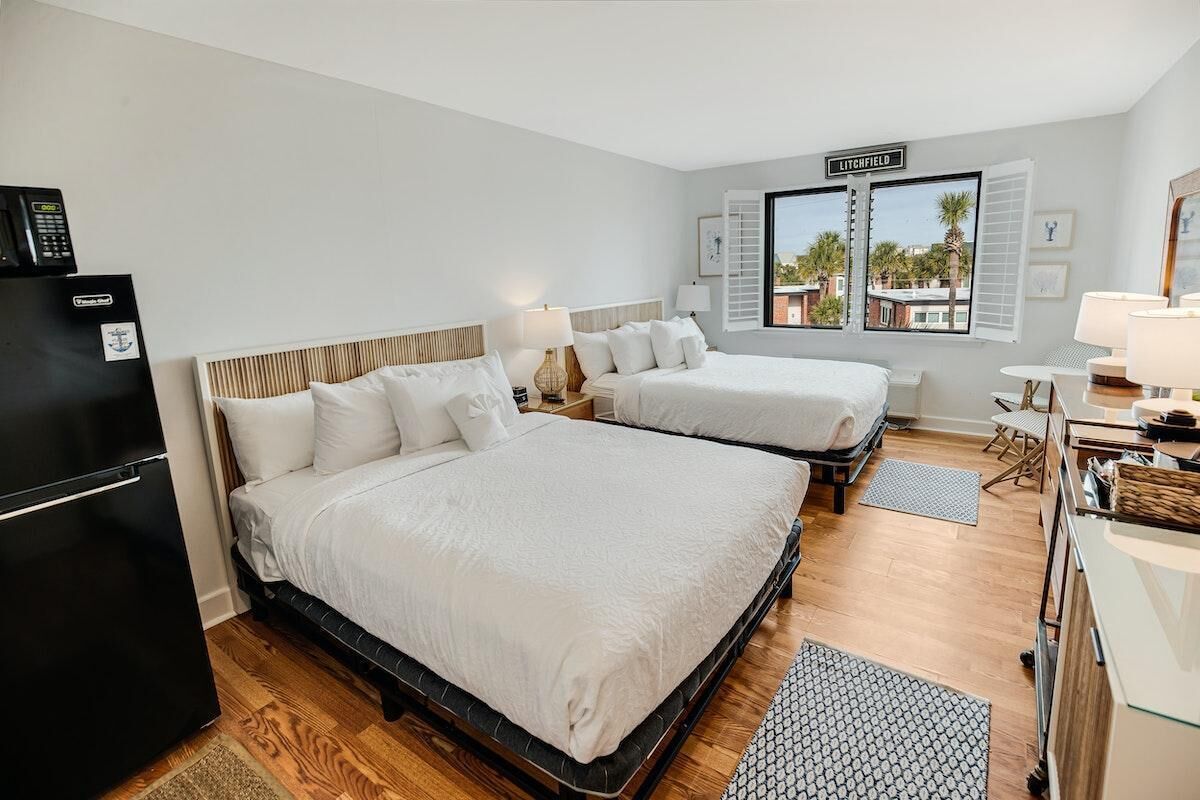 Une chambre d’hôtel avec deux lits, un réfrigérateur, un bureau avec une lampe et une fenêtre donnant sur des immeubles.