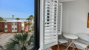 A balcony with a view of the beach and palm trees, a white table with two chairs, and a wooden floor. - Welcoming Adventure Resort View Lodge Room 3rd Flr (Pawleys Island)