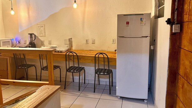 A compact kitchen with a wooden table, four chairs, a refrigerator, a microwave, and a blender. - Hostel Mar (São Luís)