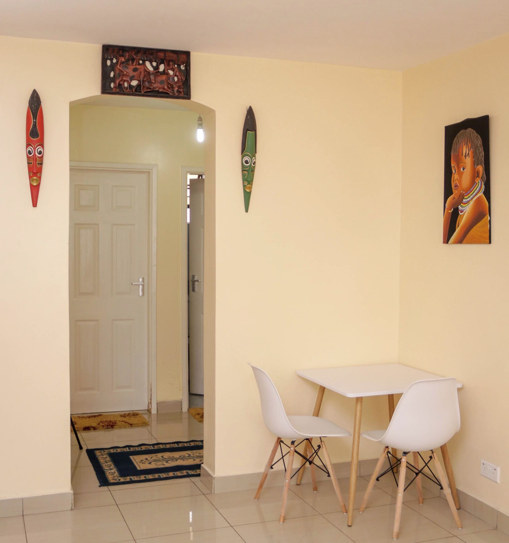 A room with a white door, a small table with two white chairs, and a painting on the wall.