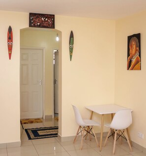 A room with a white door, a small table with two white chairs, and a painting on the wall. - Lux Suites Tulia Homestays Nakuru (Nakuru)