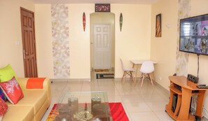 A living room with a sofa, coffee table, TV, and a small dining area. - Lux Suites Tulia Homestays Nakuru (Nakuru)