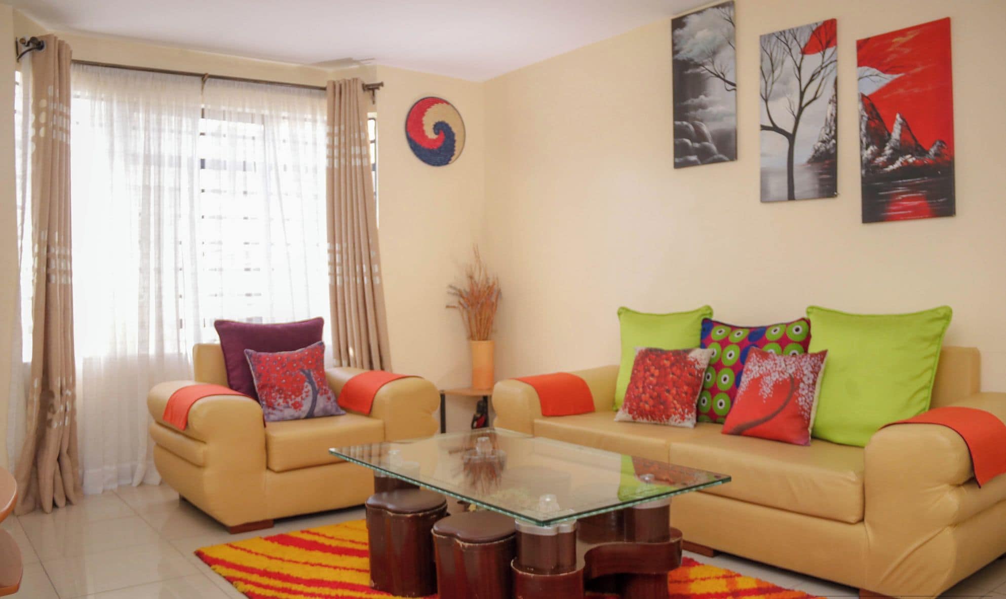 Un salón con dos sofás color beige, una mesa de centro de cristal y una alfombra a rayas roja y amarilla.