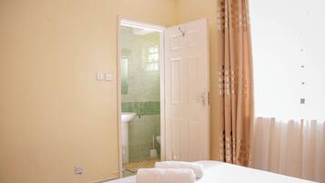 Une chambre d’hôtel avec un lit, deux serviettes, une porte donnant sur une salle de bain et une fenêtre avec des rideaux.