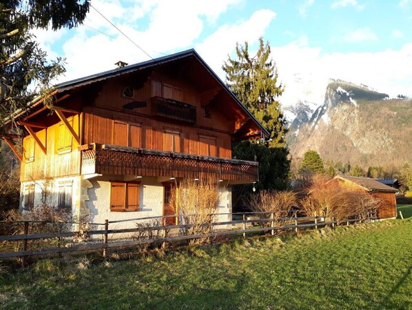 A wooden chalet with a balcony, surrounded by a wooden fence and a mountain backdrop. - Quiet T4 apartment with garden and wifi, near center and ski-bus (Samoëns)