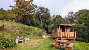 A wooden cabin with a porch and a picnic table in a grassy area surrounded by trees. - Charming Roulotte Stay: Streamside Serenity, Sauna, Massage & Ideal for Family or Friends (Ferdrupt)