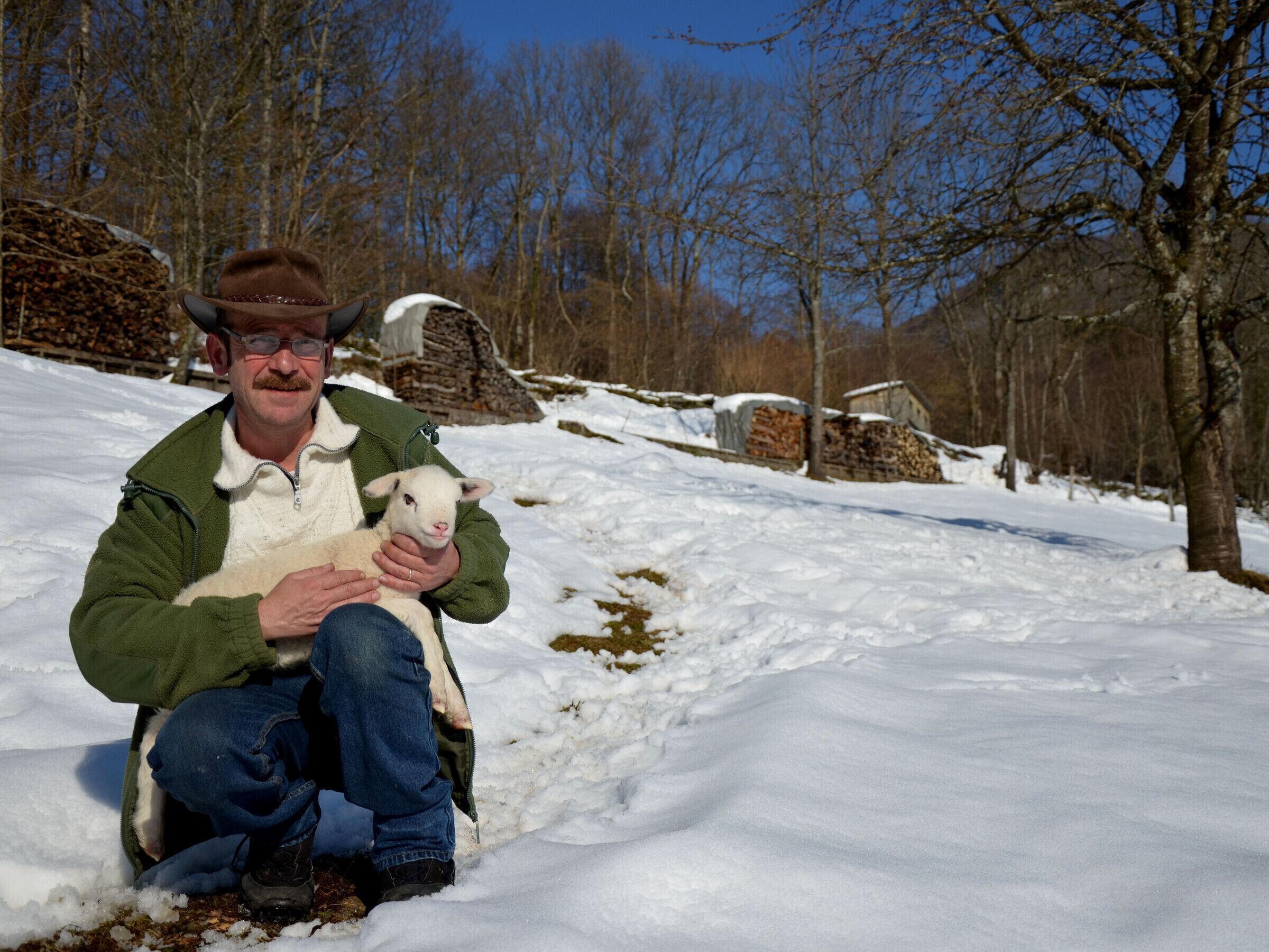 Une personne assise dans la neige, tenant un agneau.