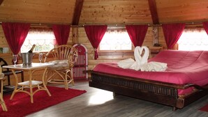 A cozy wooden cabin room with a bed, a table with a bottle of champagne, and a chair.