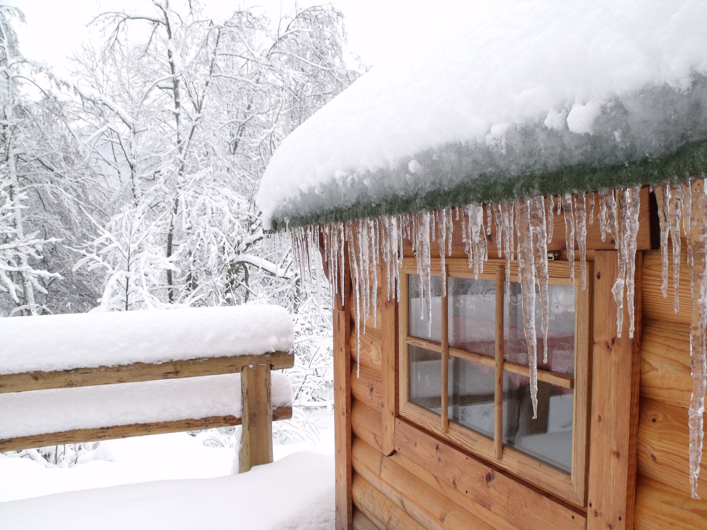 Una baita di legno con un tetto imbiancato dalla neve e stalattiti che pendono dai cornicioni.