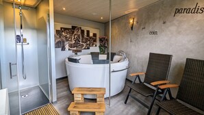 A modern bathroom with a freestanding bathtub, a wooden bench, and wicker chairs.