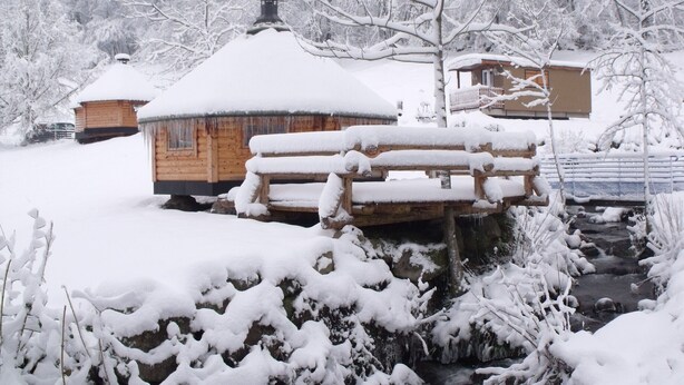 A wooden cabin with a snow-covered roof and a wooden bench in front.