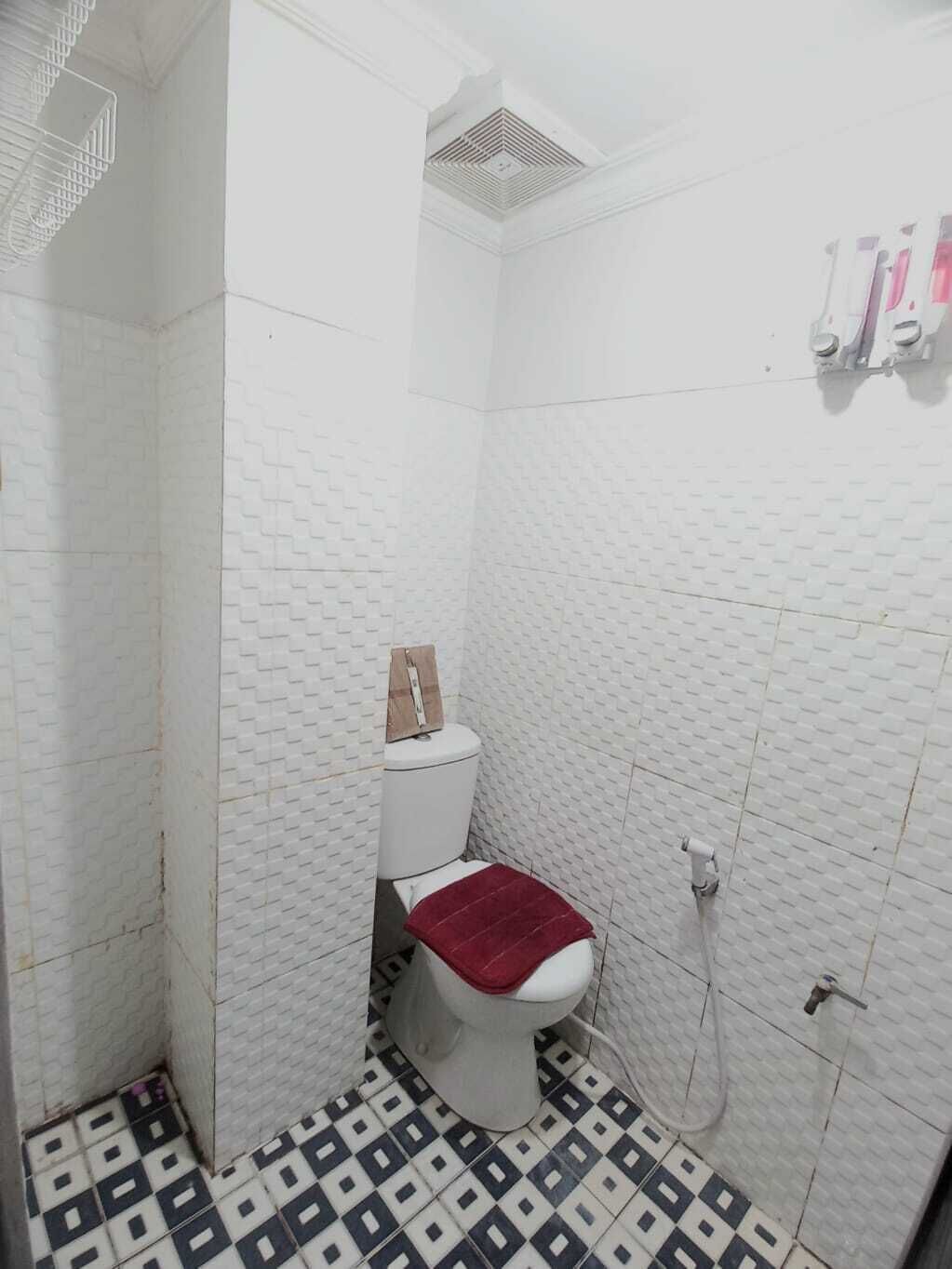 A small, narrow bathroom with a toilet, a red seat cover, and a patterned floor.