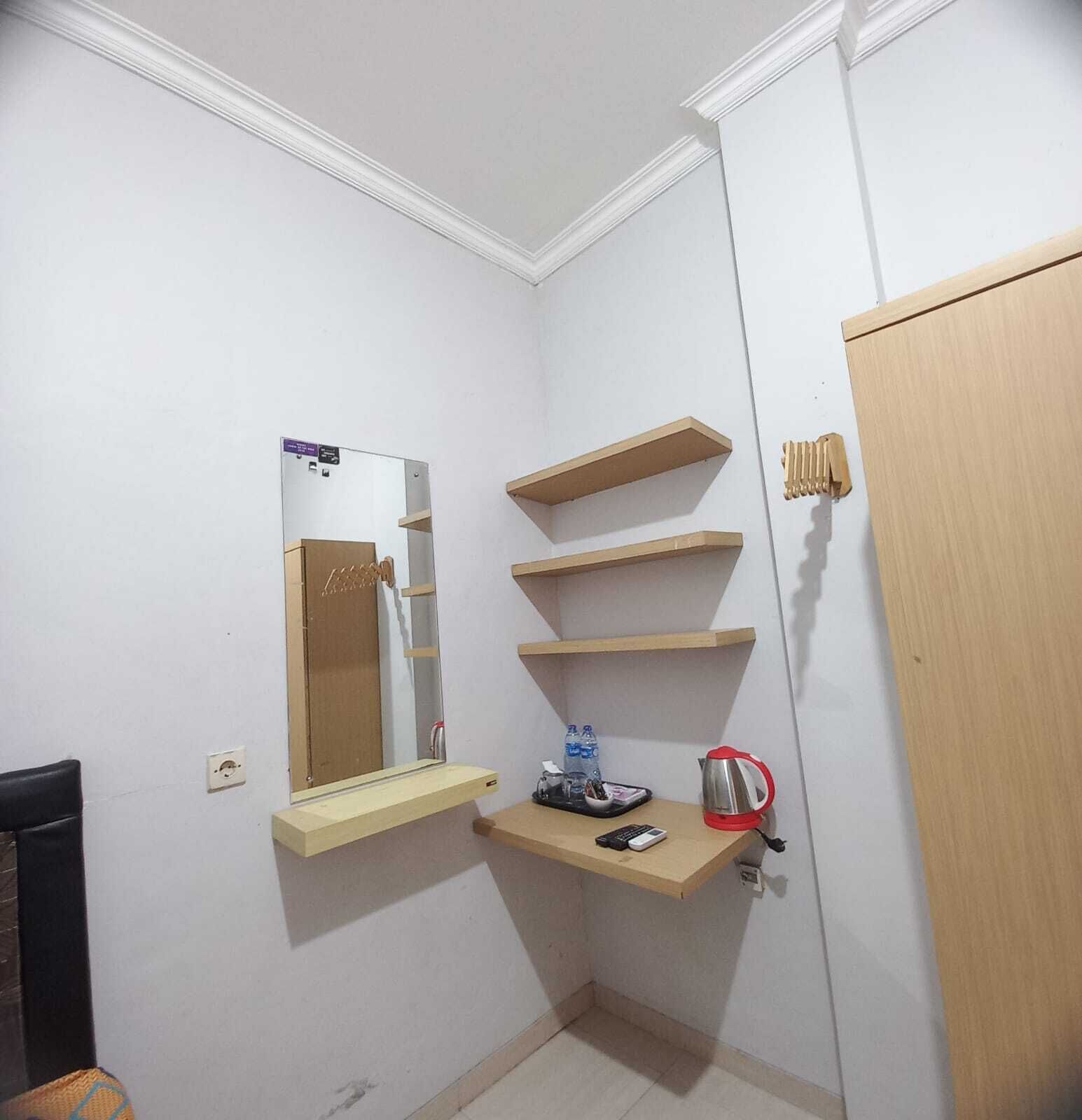 A small, clean room with a mirror, wooden shelves, a door, and a chair.