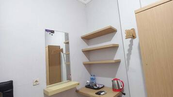 A small, clean room with a mirror, wooden shelves, a door, and a chair.