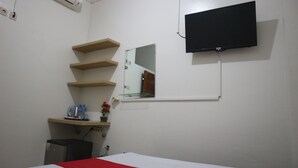 Une chambre d’hôtel avec un lit, un téléviseur fixé au mur, un miroir et un petit bureau équipé d’une bouilloire et agrémenté d’une plante.
