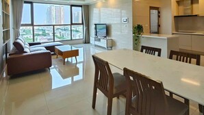 A modern living room with a sofa, dining table, and chairs. There is a TV and a plant in the room.