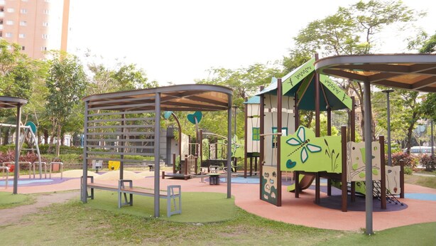 A playground with various play structures, including a climbing frame and a slide, surrounded by grass and trees.