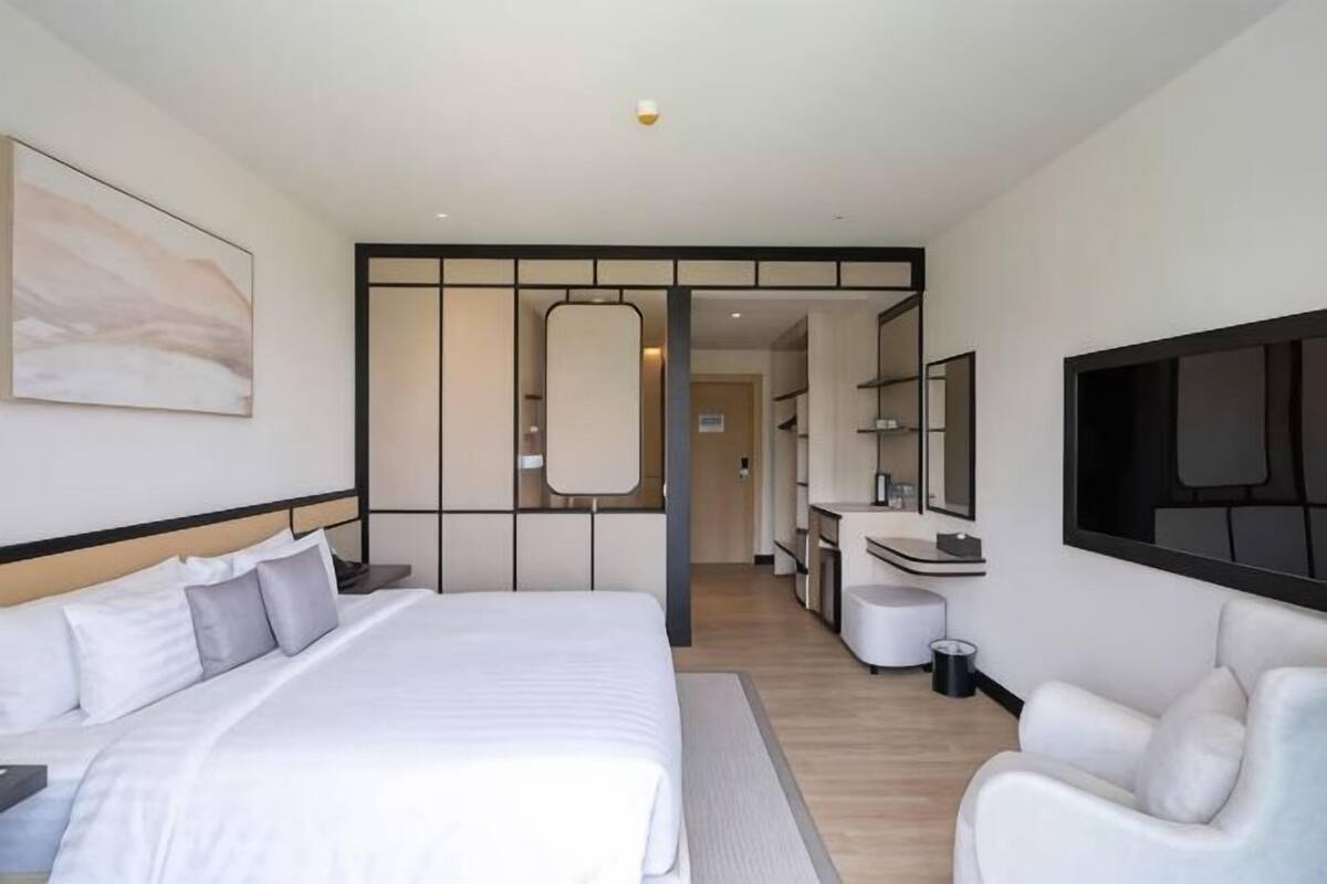 A modern hotel room with a large bed, a sitting area, a bathroom, and a mirror.