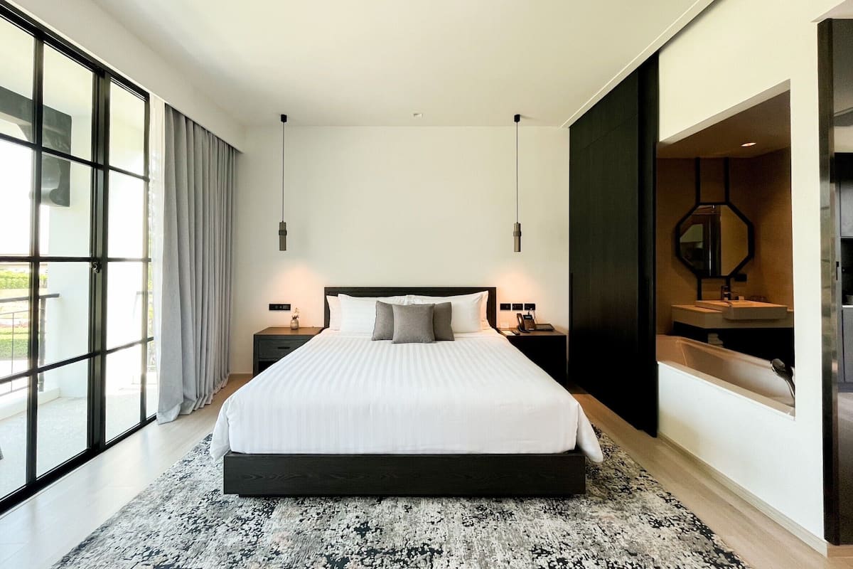 A modern bedroom with a large bed, bedside tables, a built-in wardrobe, and a large window with curtains.