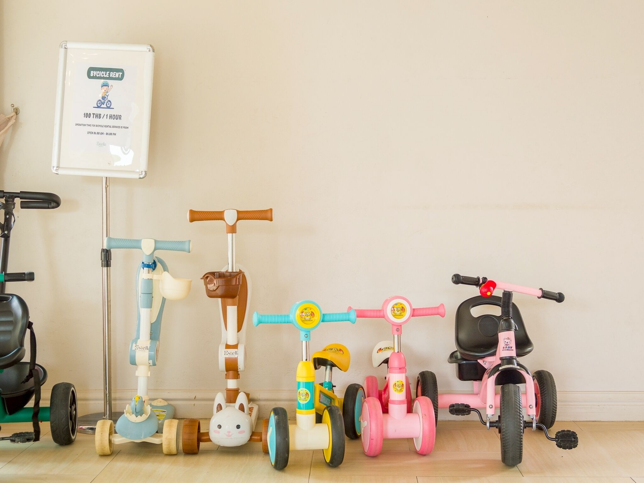 A row of children's tricycles and a bicycle rental sign on the wall.