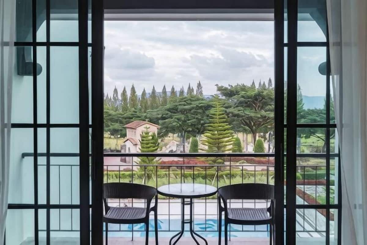 A balcony with two chairs and a table, overlooking a garden with trees and a building.