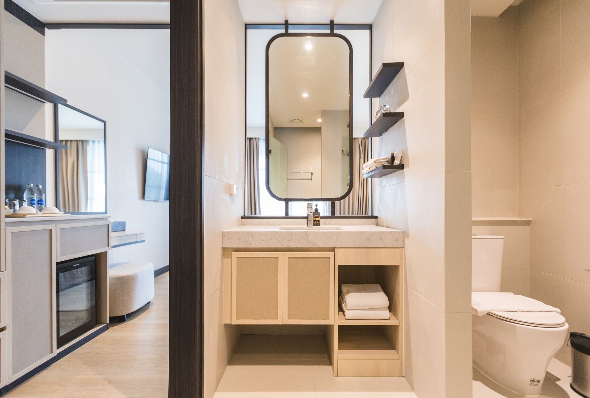 A modern bathroom with a large mirror, a sink, and a toilet. There is a cabinet with towels and toiletries.
