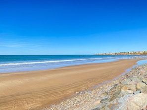 A wide sandy beach with a rocky shoreline, calm sea, and clear sky.