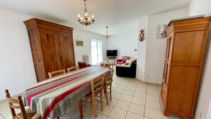 Ein Essbereich mit einem langen Tisch, Stühlen, einer Kristallleuchtre, Holzschränken und einem Fernseher im Hintergrund.
