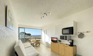 A room with a balcony, a dining area, a kitchenette, and a TV.