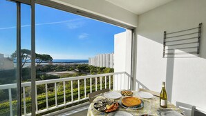 A balcony with a table set for dining, overlooking a coastal area with buildings and trees.