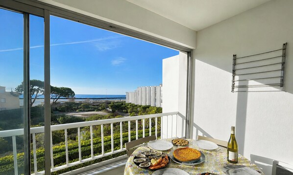 A balcony with a table set for dining, overlooking a coastal area with buildings and trees.