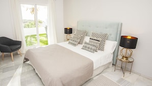 A bedroom with a large bed, two bedside lamps, a chair, and a view through a window. - Beautiful 3-bedroom apartment with terrace in Nueva Andalucía, Marbella (Marbella)