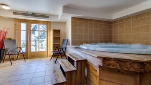 Un espace spa comprenant un banc en bois, un jacuzzi et une vue à travers une porte vitrée.