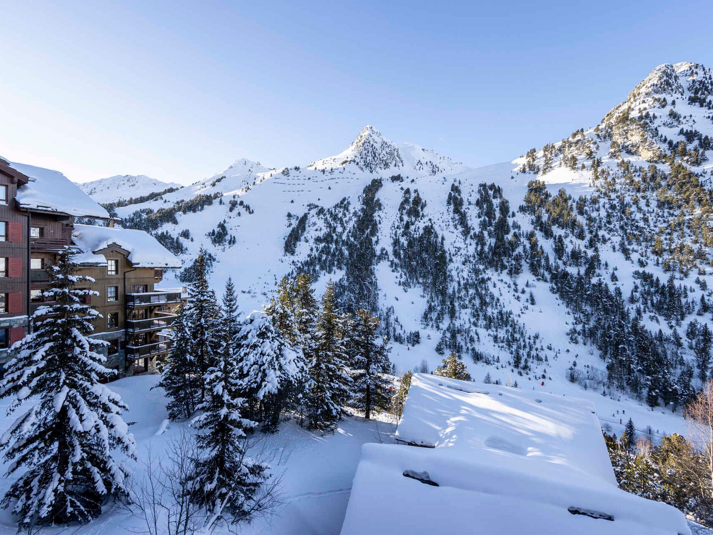 A snow-covered mountain landscape with a lodge featuring multiple balconies and a ski slope in the background.