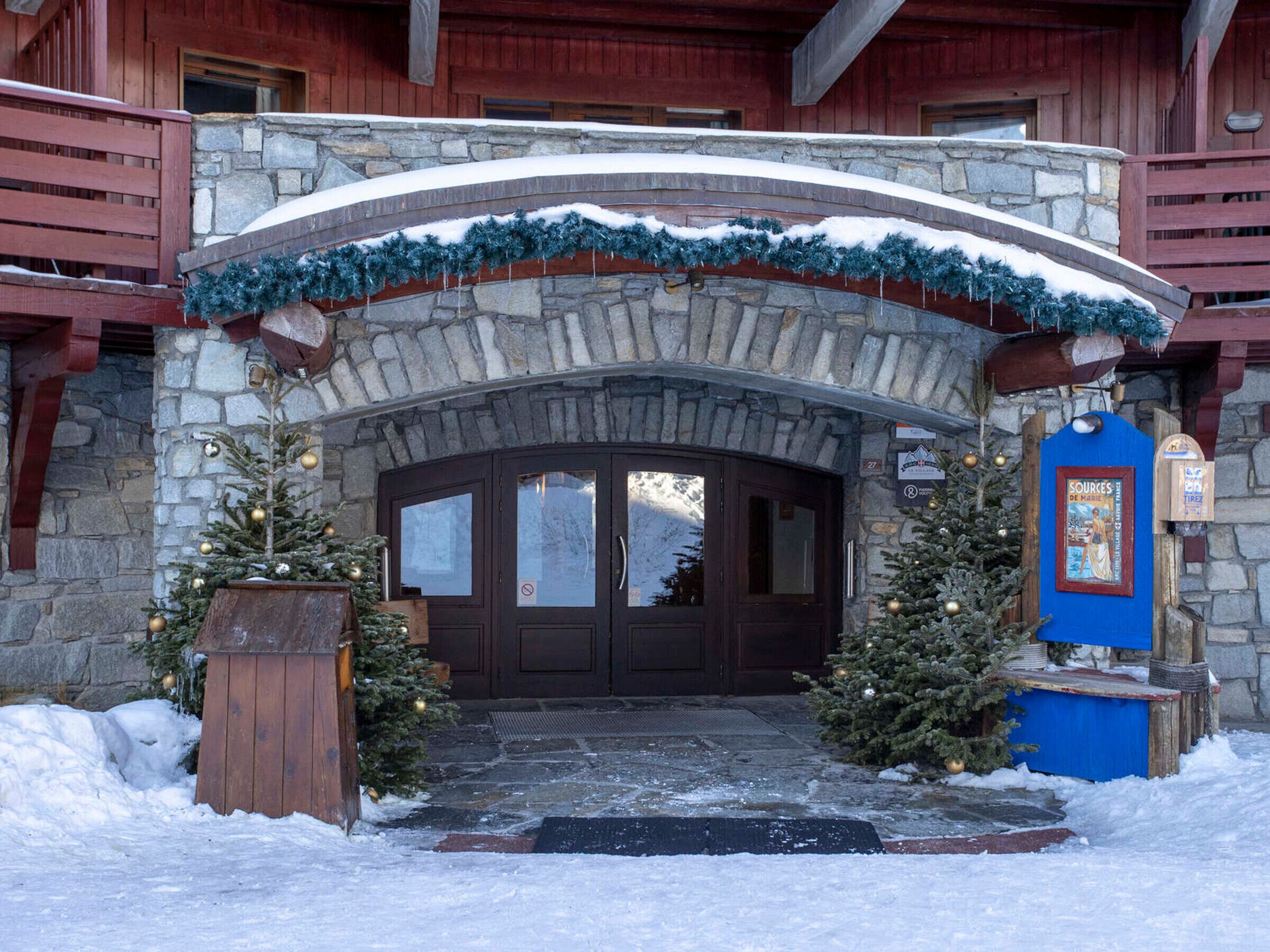 Un arco de piedra que da paso a una puerta de madera, con un árbol de Navidad y adornos a ambos lados.
