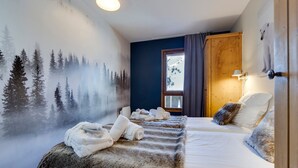 Une chambre décorée d’une fresque représentant une forêt, un lit recouvert d’un plaid en fourrure et une fenêtre donnant sur les arbres.