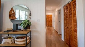 A hallway with wooden flooring, a mirror with a decorative piece, and storage baskets. - Sunny and Chair: Early Bird Special! (Oak Island)