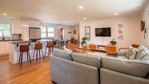 A modern kitchen with a central island, bar stools, and a dining area with chairs. - Sunny and Chair: Early Bird Special! (Oak Island)