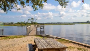 A wooden dock extending into a calm lake with a picnic table nearby. - Sunny and Chair: Early Bird Special! (Oak Island)