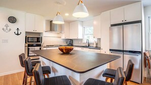 A modern kitchen with a central island, stainless steel appliances, and pendant lighting. - Sunny and Chair: Early Bird Special! (Oak Island)
