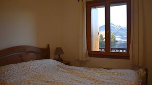 Ein Schlafzimmer mit einem hölzernen Bett, einem Nachttisch mit Lampe und einem Fenster mit Blick auf die Berge.