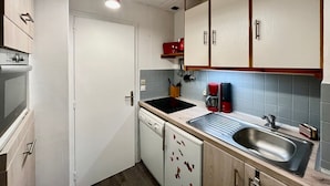 A compact kitchen with white cabinets, a stainless steel sink, a red coffee maker, and a dishwasher. - T2 Apartment in Mont-Dore, 4 pers, pets allowed, WiFi (Mont-Dore)