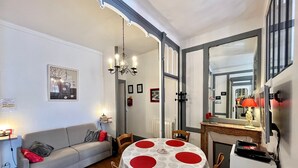 A dining area with a round table, chairs, a sofa, and a chandelier. - T2 Apartment in Mont-Dore, 4 pers, pets allowed, WiFi (Mont-Dore)