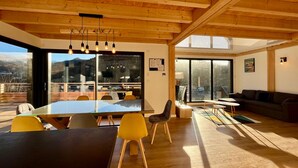 Ruime eethoek met een grote tafel en stoelen, een houten plafond en grote ramen met uitzicht op de bergen.