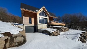 Een modern huis met een stenen fundering, grote ramen en een houten terras.
