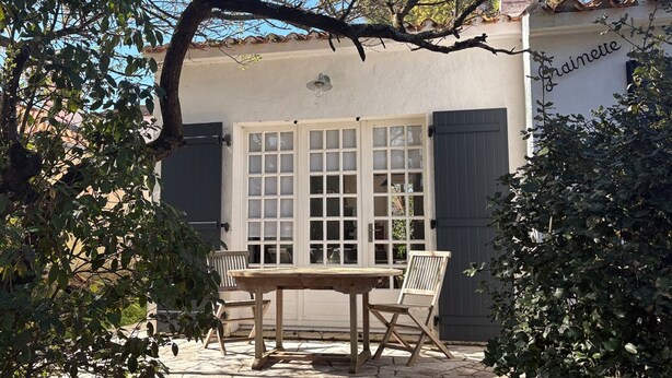 Un patio con una mesa y sillas de madera, una ventana con contraventanas y un letrero que dice "Gaiette".