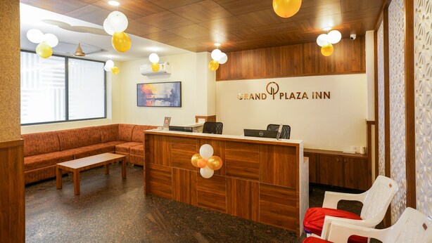 A reception area with a wooden reception desk, a sofa, and chairs. - Grand Plaza Inn (Tirur)